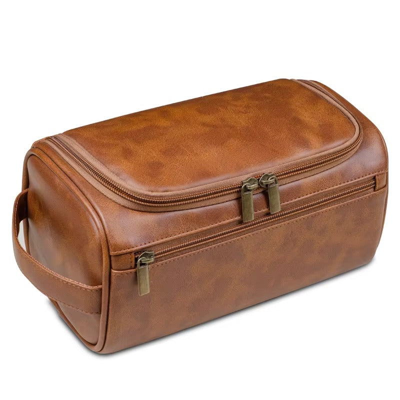 Large cognac brown PU leather Dopp Kit toiletry bag with T-shape hang loop and dual antique brass zippers, shown at 45-degree angle on white background